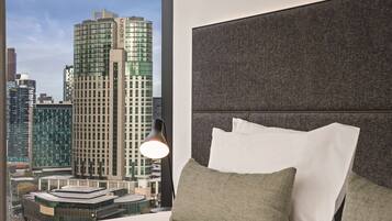 A hotel room with a city view, a modern bed, and a large window.