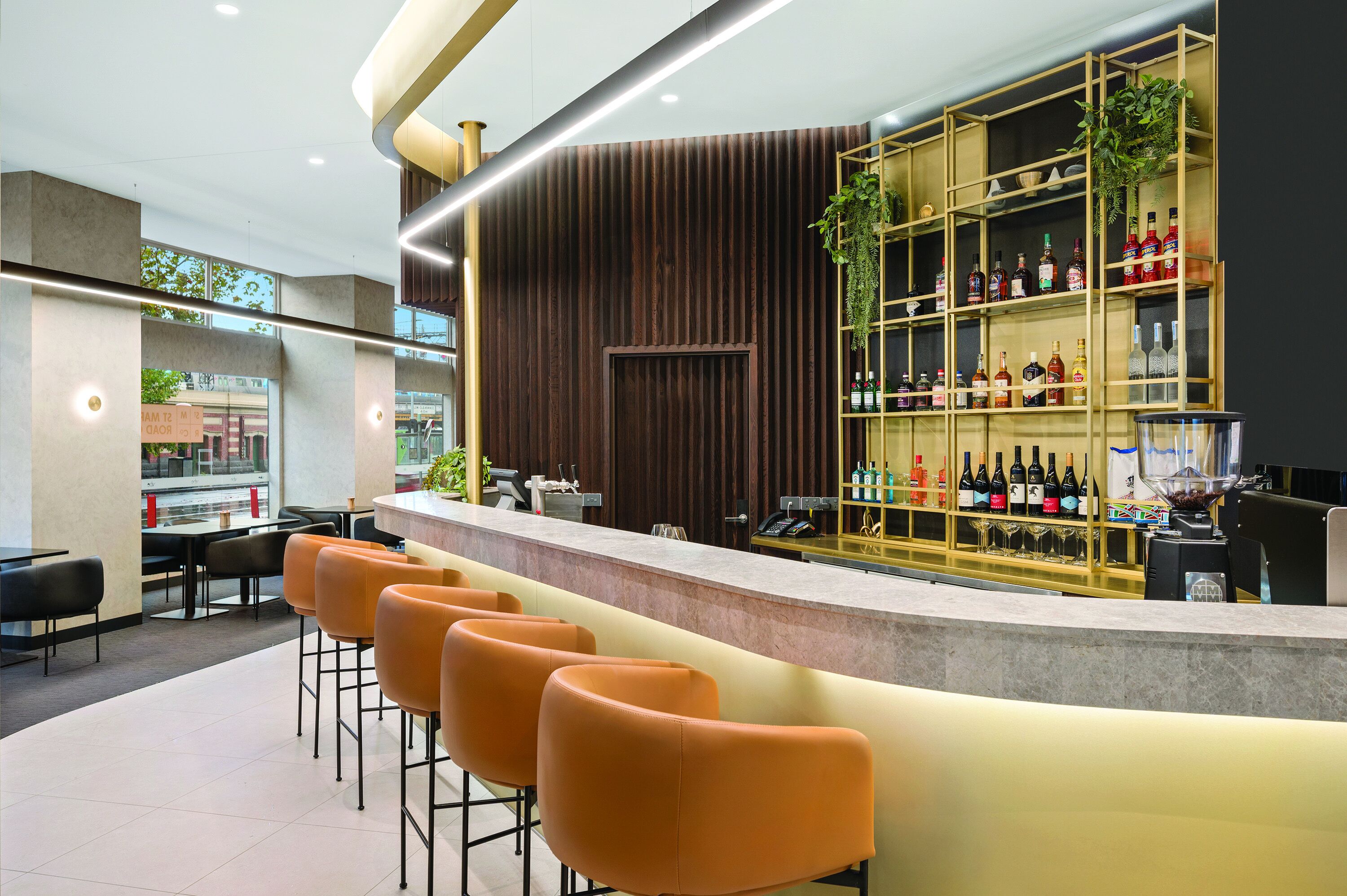 Zona de bar moderna con una barra larga, varios taburetes naranjas y una vitrina para vinos.