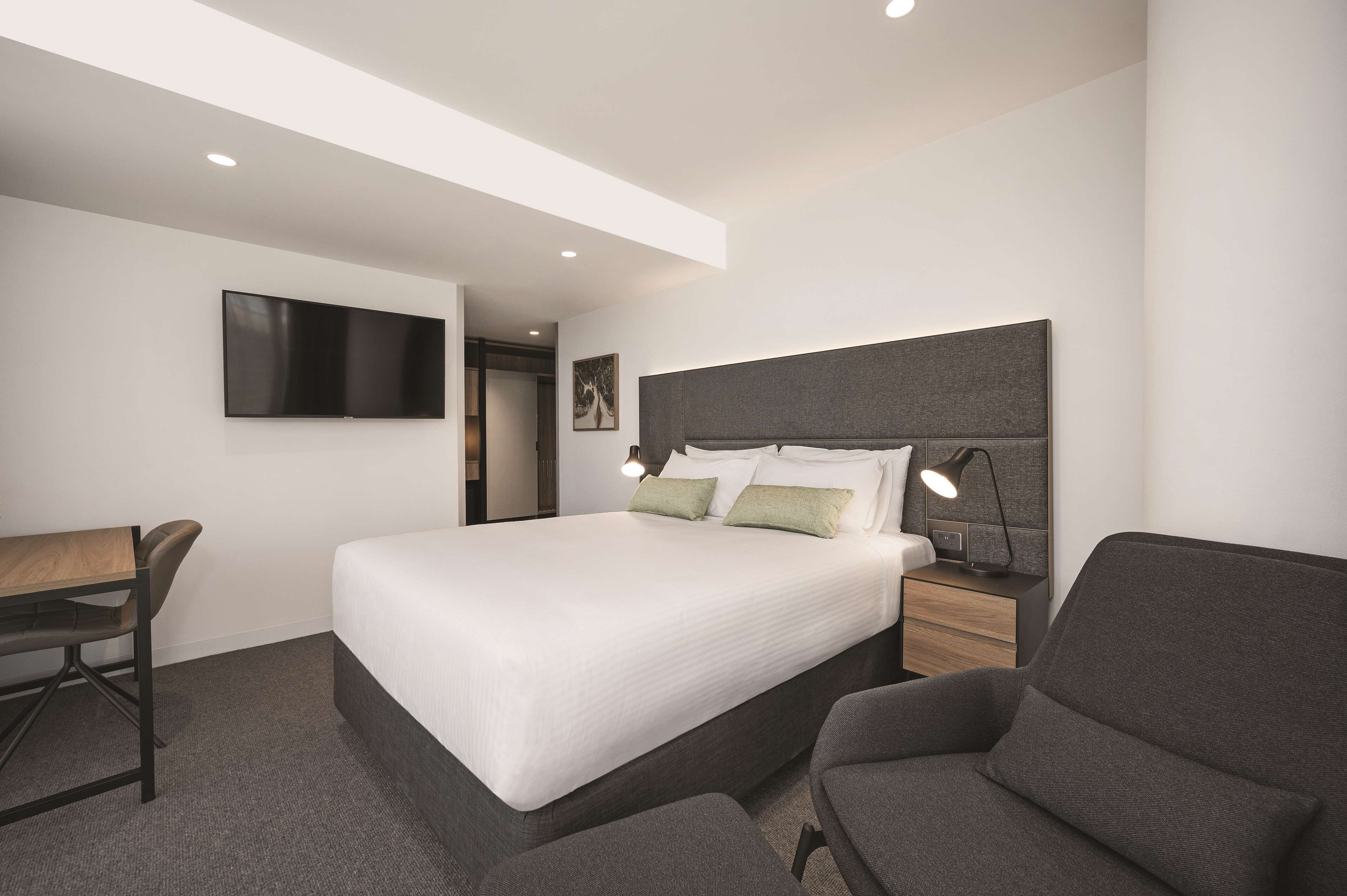 Una habitación de hotel moderna con una cama grande, un escritorio, una silla, un televisor y una lámpara de noche.