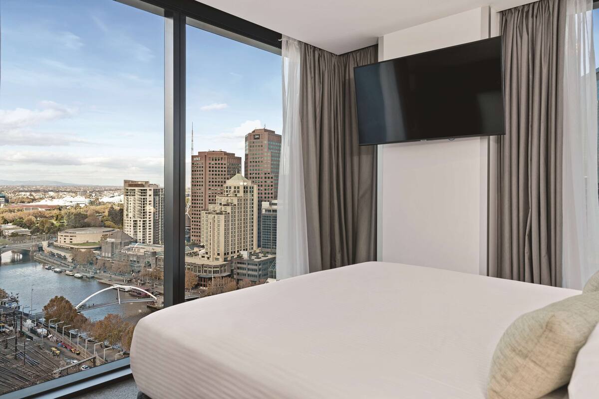 Ein Hotelzimmer mit einem großen Bett, einem Flachbildfernseher und Blick auf eine Stadtlandschaft mit einem Fluss und Brücken.