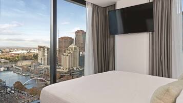 A hotel room with a large bed, a flat-screen TV, and a view of a cityscape including a river and bridges.