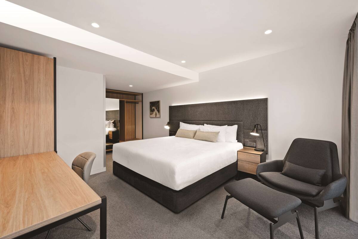 Ein modernes Hotelzimmer mit einem großen Bett, einem Schreibtisch, einem Stuhl und einem Nachttisch mit Lampe.