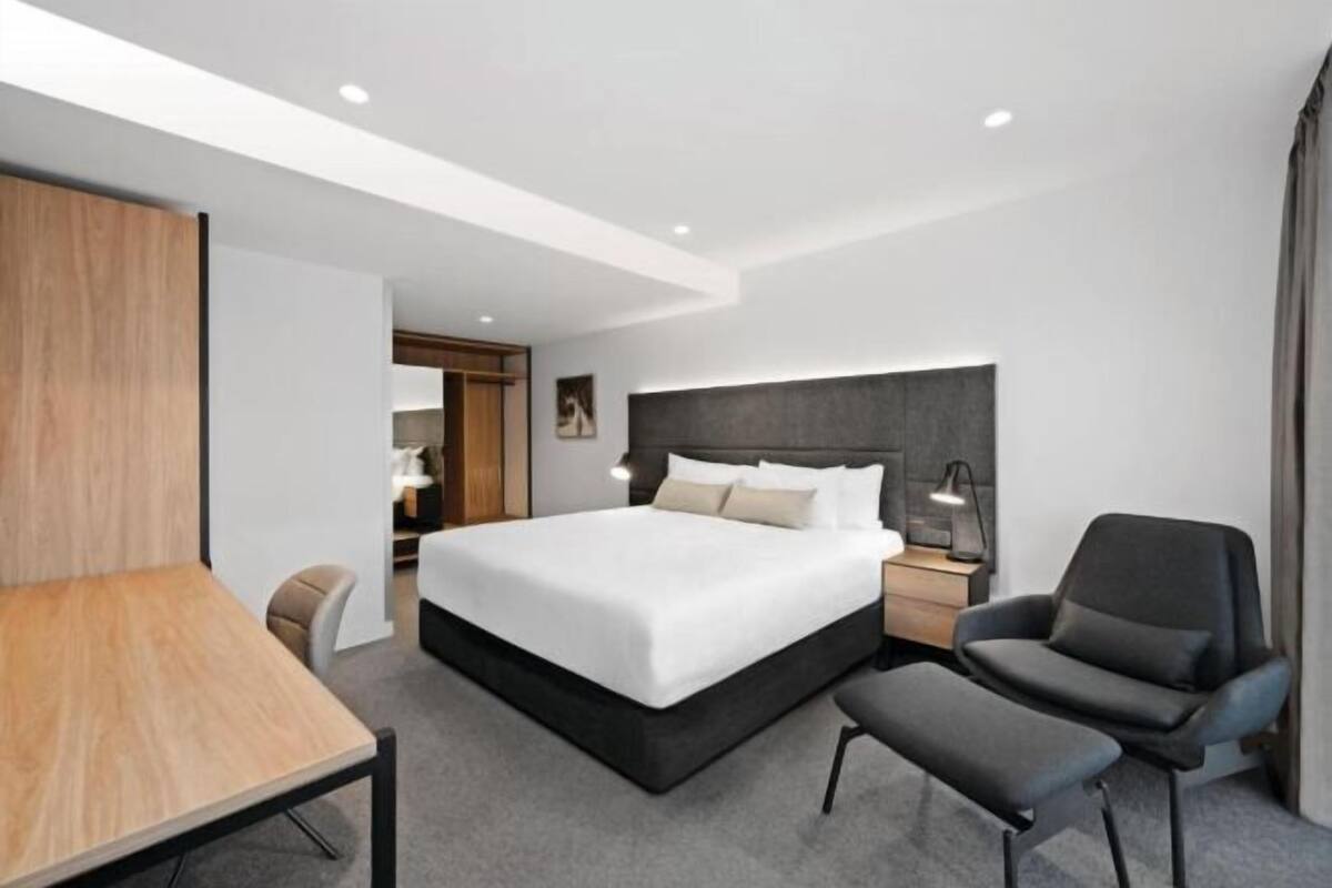 Ein modernes Hotelzimmer mit einem großen Bett, einem Schreibtisch, einem Sessel und einem Nachttisch.