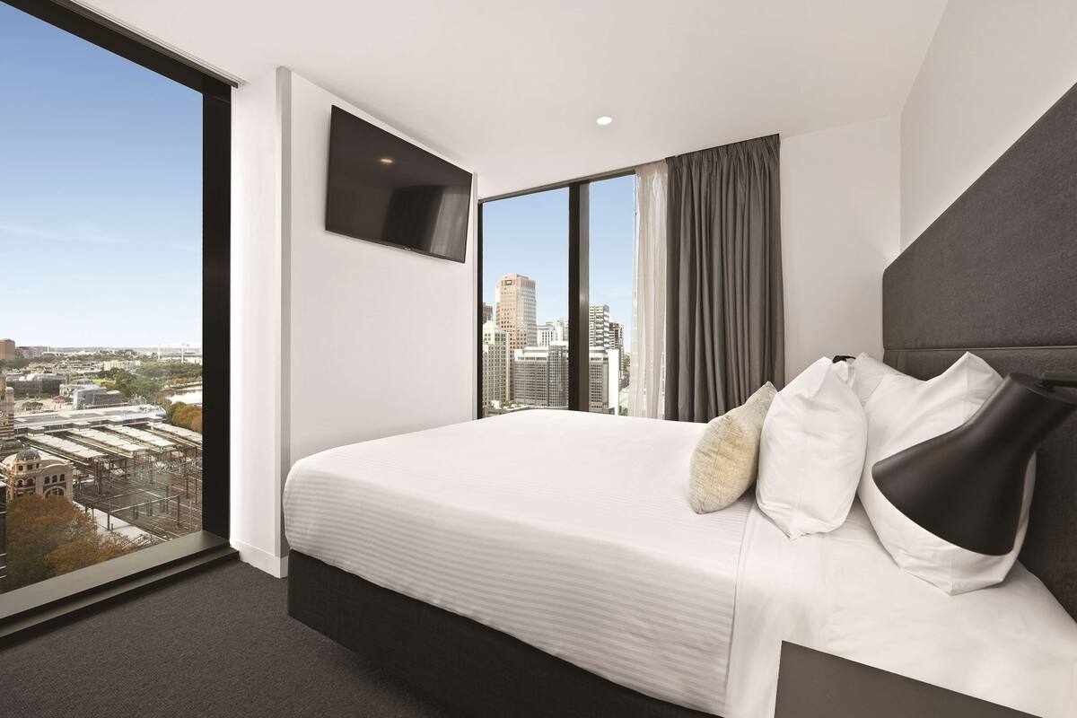 Ein modernes Hotelzimmer mit einem großen Bett, einem flachbildfernseher an der Wand und Blick auf die Stadt durch große Fenster.