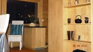 Un intérieur en bois comprenant un coin cuisine, une chaise avec un coussin bleu et des étagères remplies de divers objets.