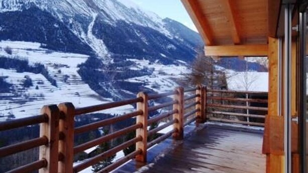 Un balcon en bois avec une balustrade en métal, donnant sur un paysage montagneux enneigé.