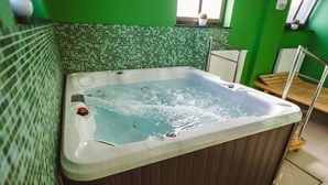 Un bain à remous dans une pièce aux murs verts et au dosseret carrelé.