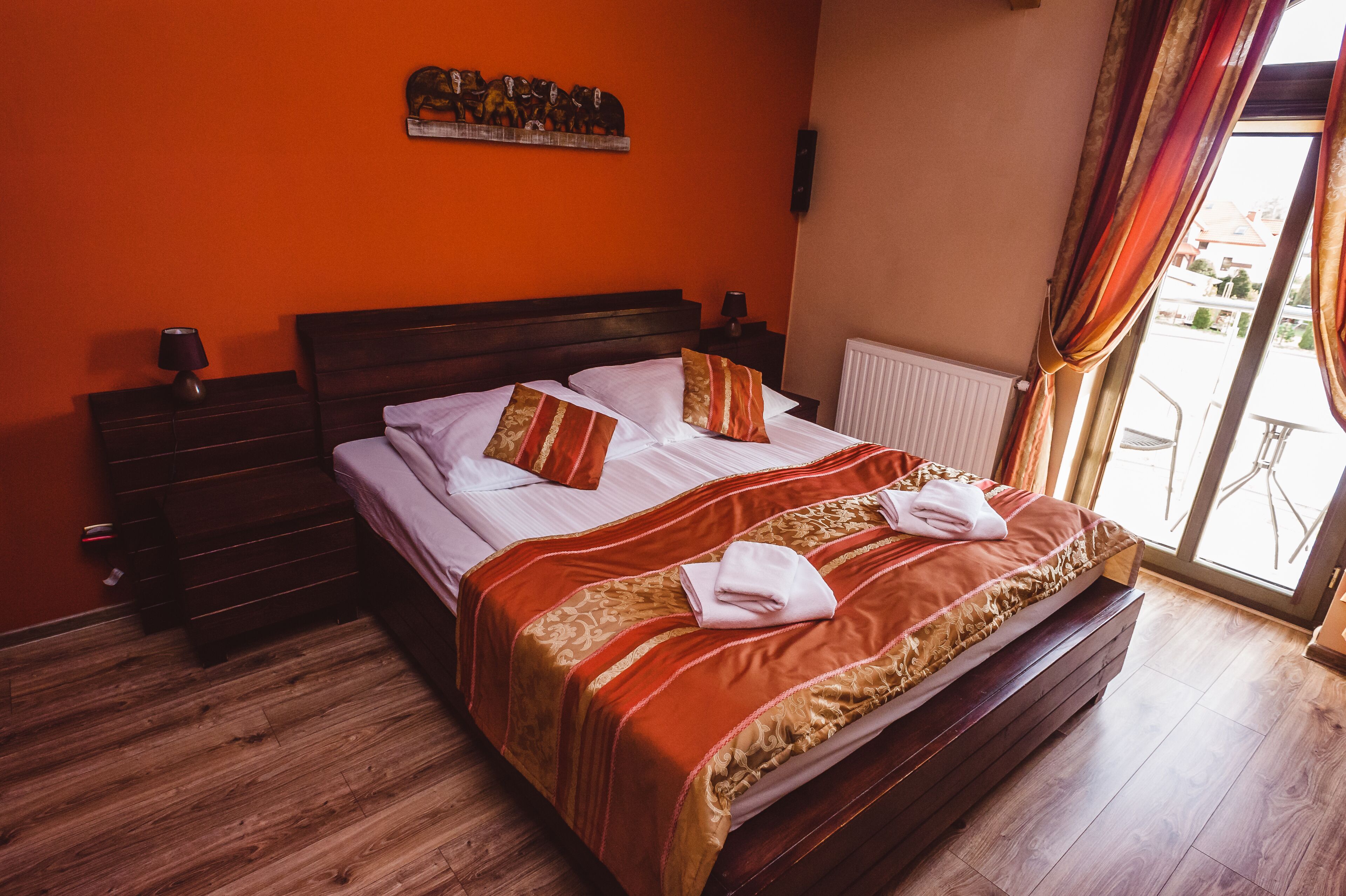 Habitación de hotel con una cama de madera, paredes anaranjadas y vistas al exterior.