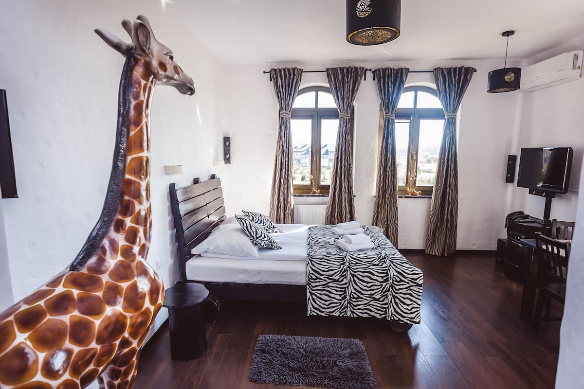 Un dormitorio con una escultura de jirafa, una cama con ropa de cama a cuadros de cebra y un televisor.