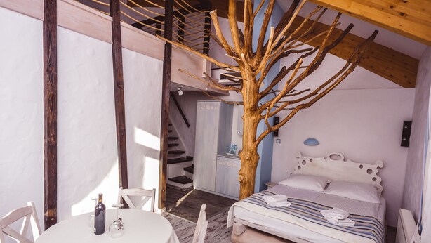 Une chambre à coucher comprenant un lit, une sculpture en bois représentant un arbre, un escalier et un coin repas avec une table et des chaises.