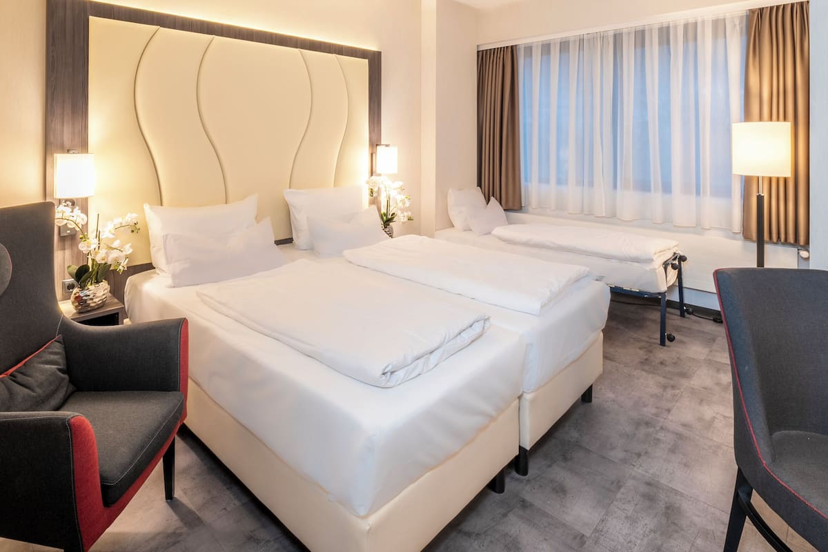 A hotel room with two beds, a sofa, a chair, and a large headboard.
