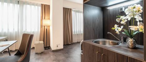 Una habitación de hotel moderna con comedor, kitchenette y un amplio ventanal con cortinas.