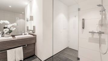 Un baño moderno con cabina de ducha de vidrio, tocador con espejo y un jarrón de flores blancas.