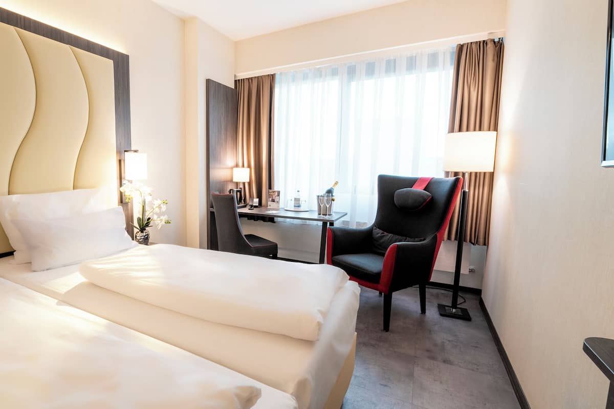 A hotel room with two beds, a desk, a chair, and a window with curtains.