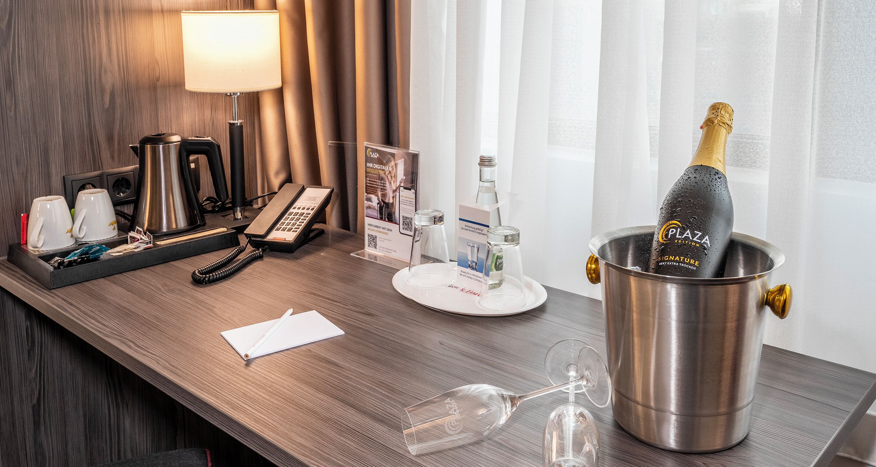 A hotel reception desk with a champagne bottle in a bucket, a telephone, a notepad, and a glass.