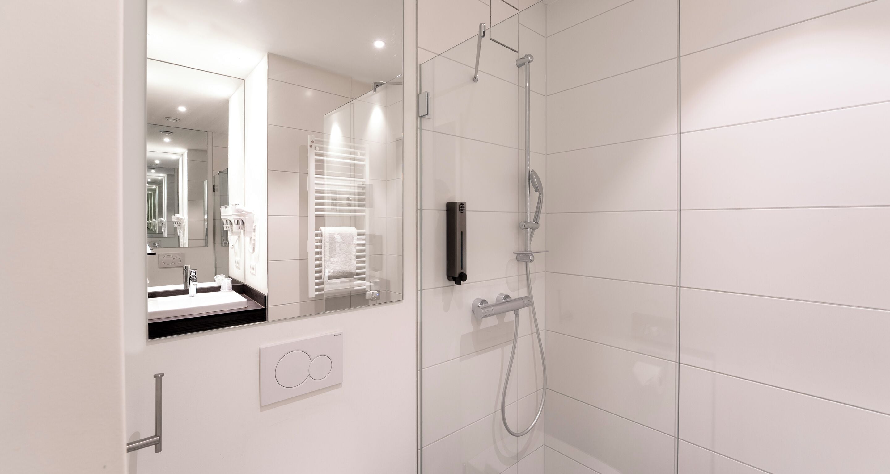 A modern bathroom with a glass shower enclosure, a white tiled wall, and a mirror reflecting the bathroom.