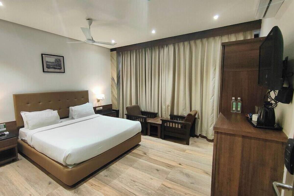 A hotel room with a large bed, a desk, a chair, a television, and a ceiling fan.