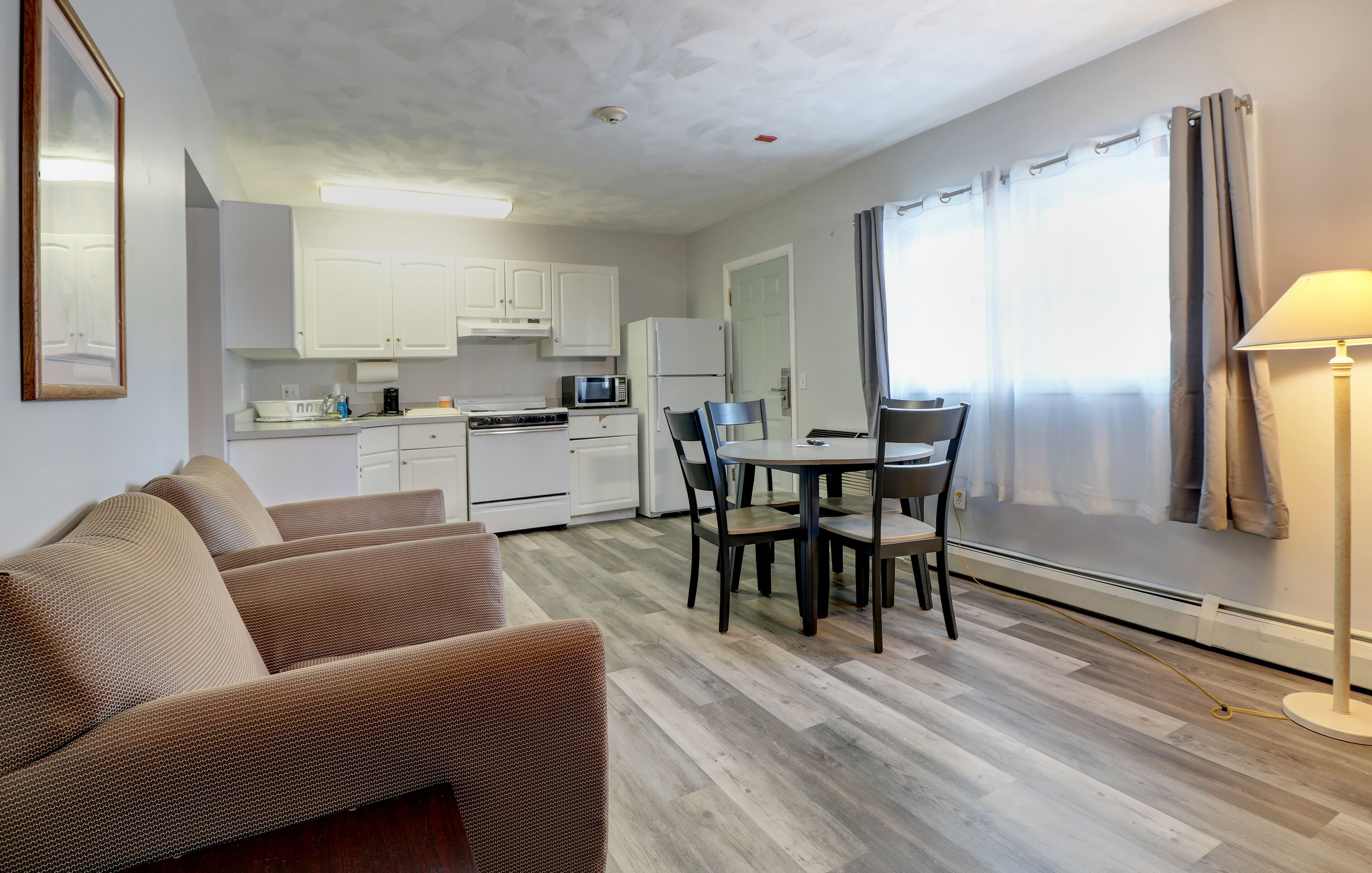 A compact living space with a kitchenette, a dining area with a table and chairs, a sofa, and a lamp.