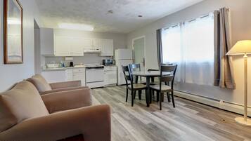 A compact living space with a kitchenette, a dining area with a table and chairs, a sofa, and a lamp.