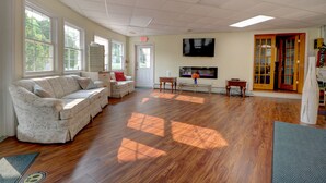 A spacious room with a wooden floor, a sofa, a TV, and a door leading to another area. - Hamilton Village Inn (North Kingstown)