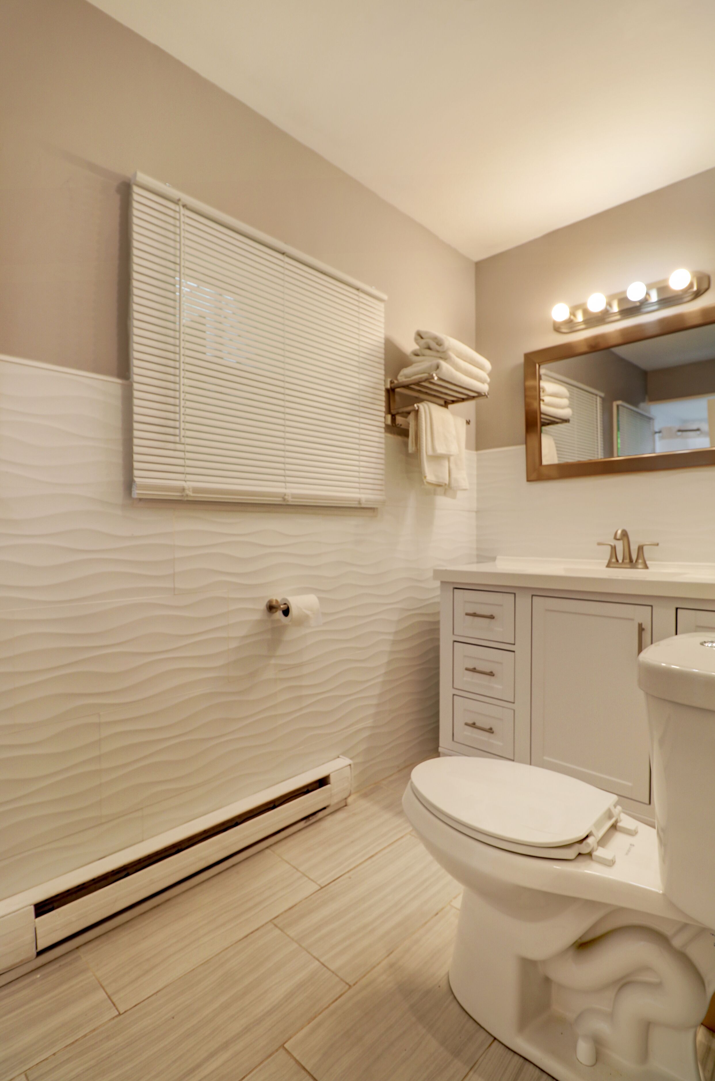 A bathroom with a toilet, sink, vanity, towel rack, and a window with blinds.