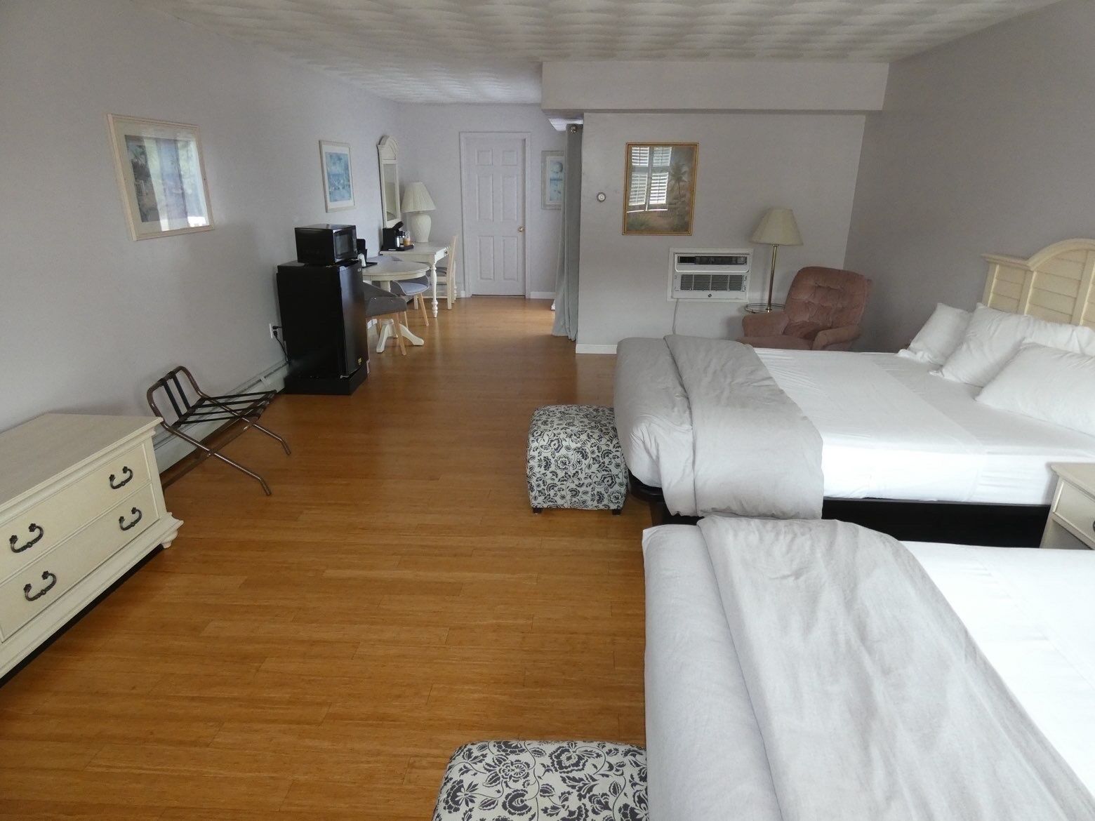 A hotel room with two beds, a desk, a chair, a dresser, and a television.