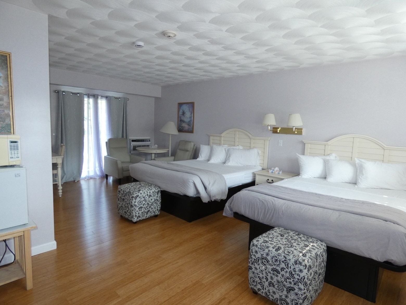 A hotel room with two beds, a desk, a chair, a lamp, and a painting on the wall.