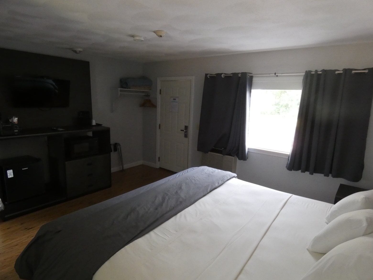 Une chambre d’hôtel comprenant un lit, un téléviseur fixé au mur, un bureau avec une chaise et une fenêtre avec des rideaux.