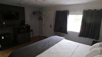 Habitación de hotel con cama, televisión montada en la pared, escritorio con silla y ventana con cortinas.
