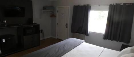 Une chambre d’hôtel comprenant un lit, un téléviseur fixé au mur, un bureau avec une chaise et une fenêtre avec des rideaux.