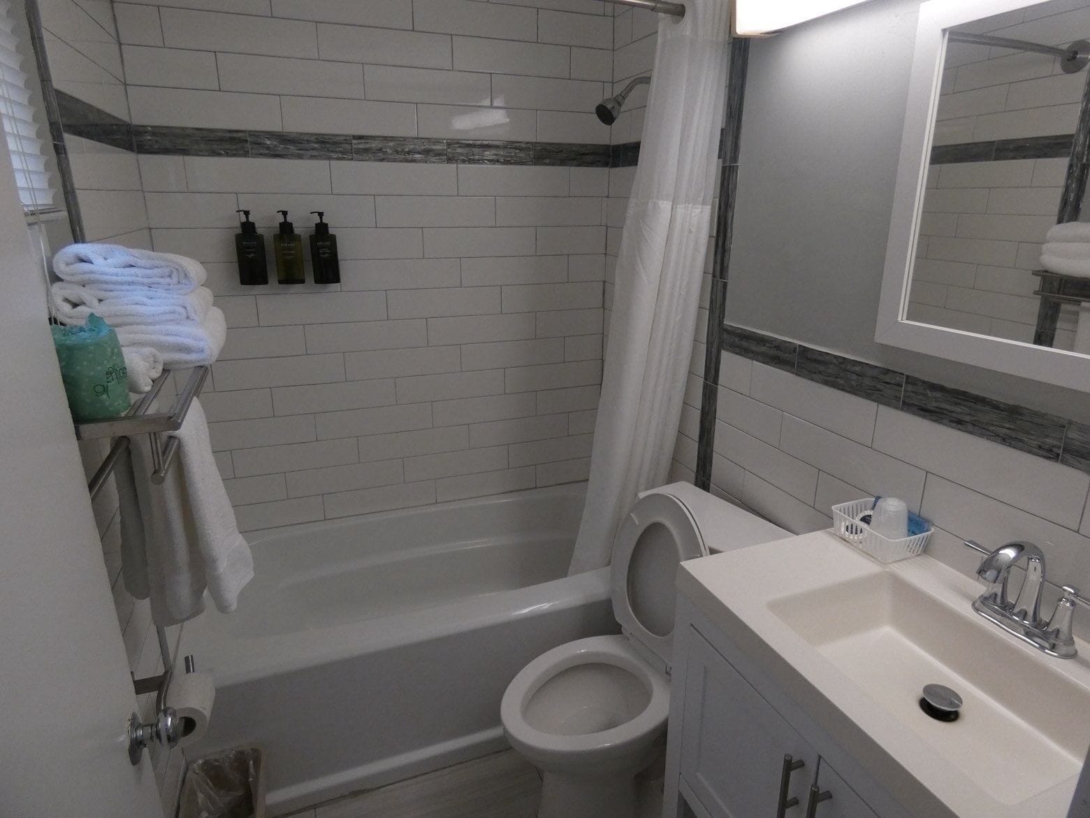 A bathroom with a bathtub, toilet, and sink. There are towels and toiletries on a shelf.