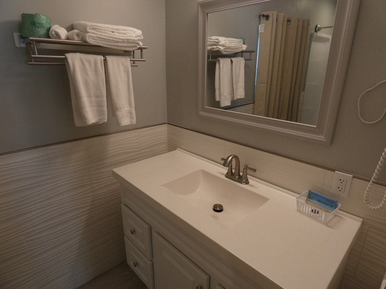 Une salle de bain avec un lavabo blanc, un miroir et un porte-serviettes sur lequel sont pliées des serviettes.