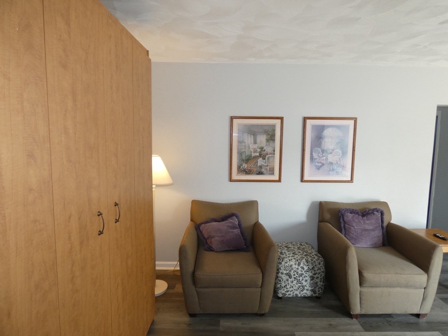 Een kamer met twee fauteuils, een houten garderobe en twee ingelijste foto’s aan de muur.