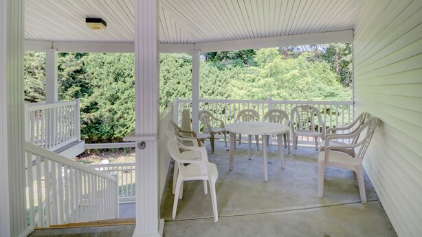 A covered porch with white railings and plastic chairs, overlooking a lush green landscape. - Hamilton Village Inn (North Kingstown)
