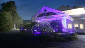 A building with a well-lit entrance and a landscaped garden area. - Hamilton Village Inn (North Kingstown)