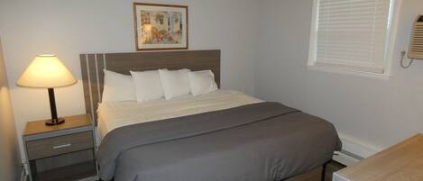 A bedroom with a bed, bedside table, lamp, and a window with blinds.