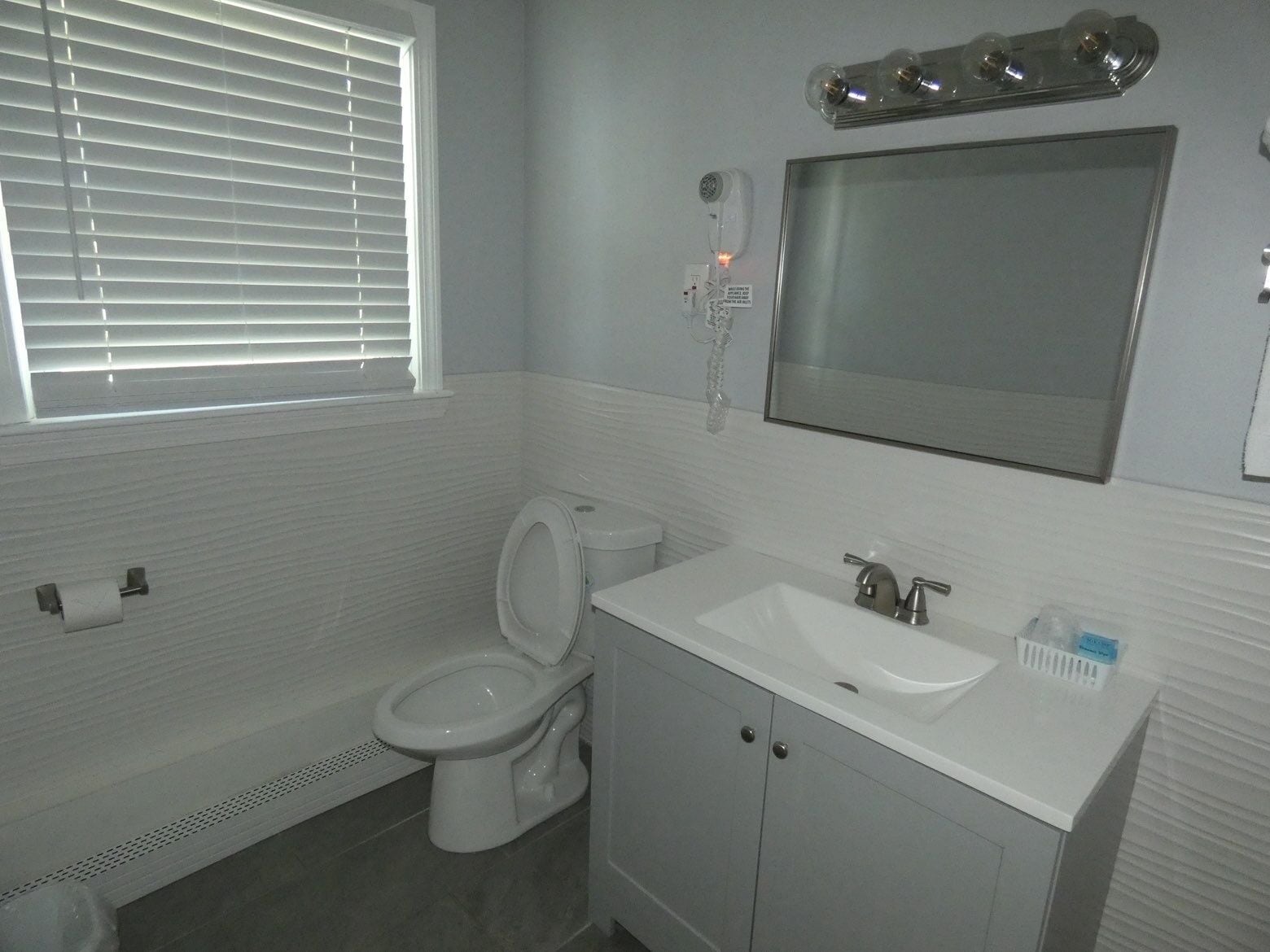 Een badkamer met toilet, wastafel, spiegel en een raam met zonwering.