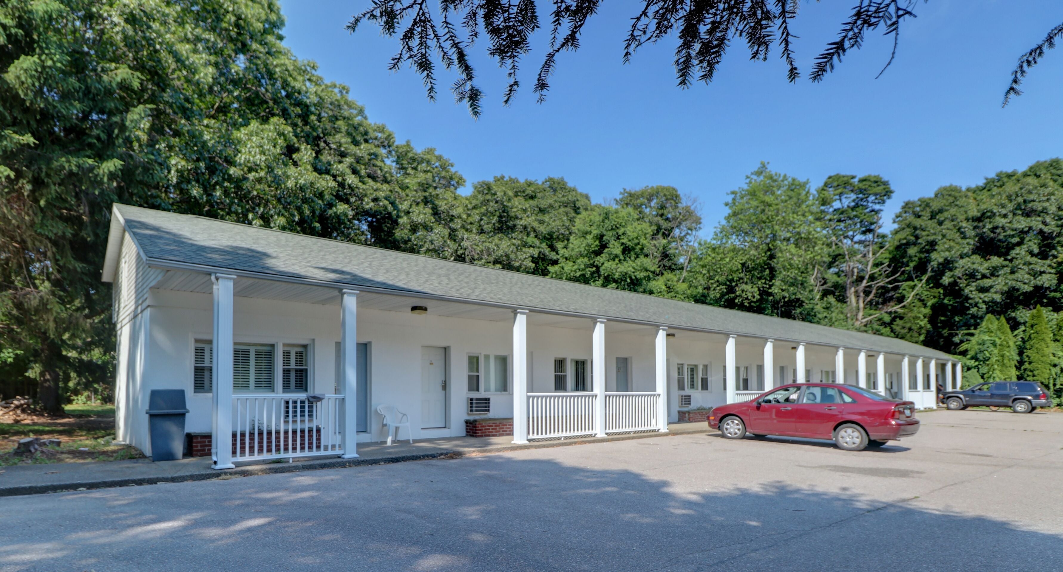 A motel with a covered parking area, a red car parked inside, and a row of white columns supporting the roof.