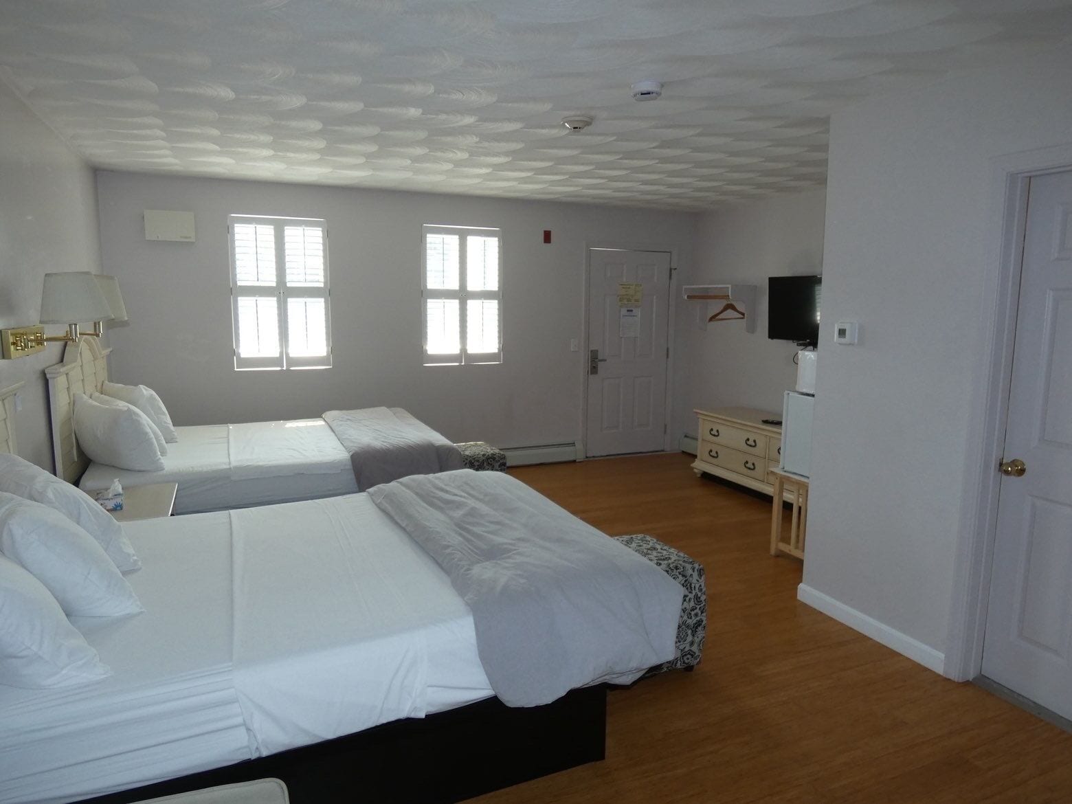 A hotel room with two beds, a dresser, a television, and a door.