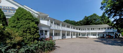 A two-story motel with a covered parking area and a large tree in front.