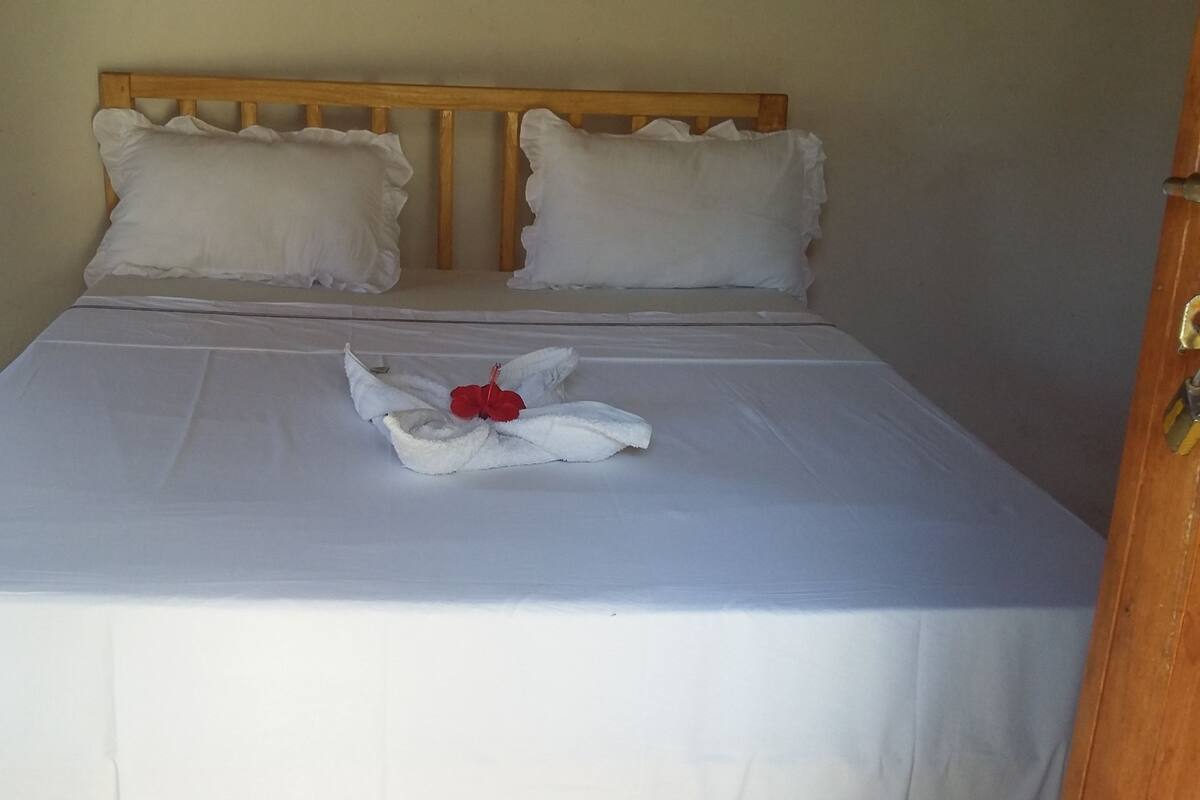 Un lit bien fait, avec du linge de lit blanc et un bouquet de fleurs rouges en guise de décoration centrale.