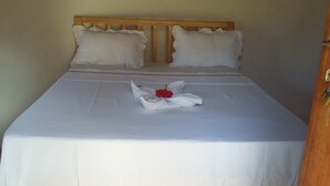 A neatly made bed with white linens and a red flower centerpiece.
