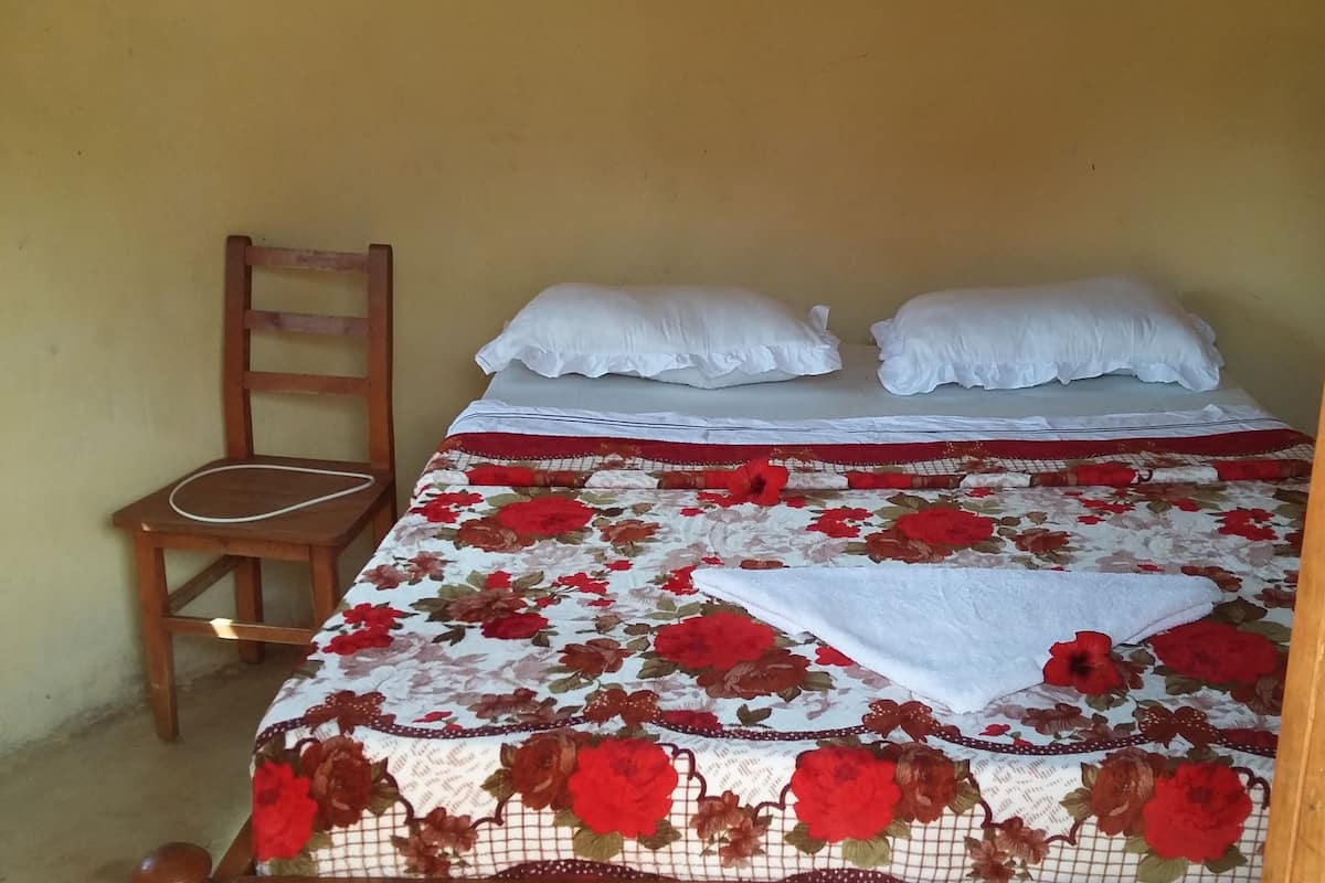 Un lit simple avec une couvre-lit à motifs floraux, des oreillers blancs et une chaise en bois.
