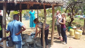A group of people around a traditional cooking setup with pots and a fire.