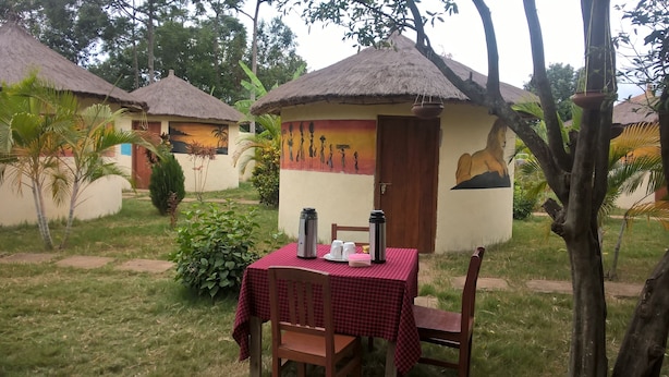 A thatched-roof hut with a mural, a table with a red checkered tablecloth, and two thermos flasks.