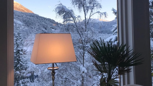 A room with a large window offering a view of snow-covered mountains and trees. - Førde Pensjonat (Sunnfjord)