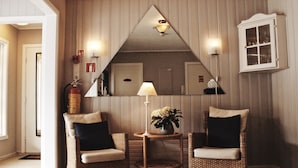 A corner room with two wicker chairs, a small table with a lamp and flowers, a mirror, and a cabinet. - Førde Pensjonat (Sunnfjord)