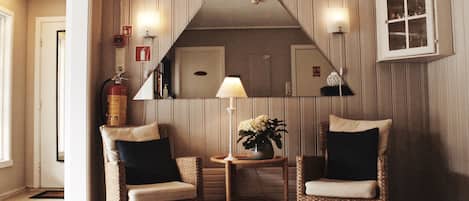 Una habitación de esquina con dos sillones de mimbre, una mesita con lámpara y flores, un espejo y un armario.