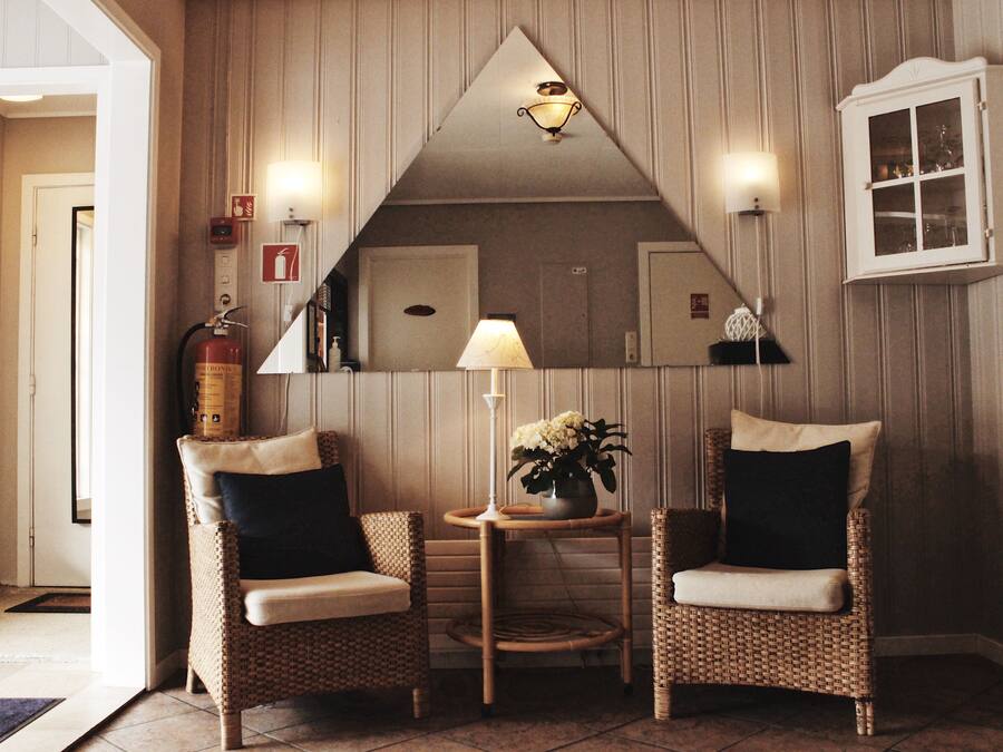 Una habitación de esquina con dos sillones de mimbre, una mesita con lámpara y flores, un espejo y un armario.