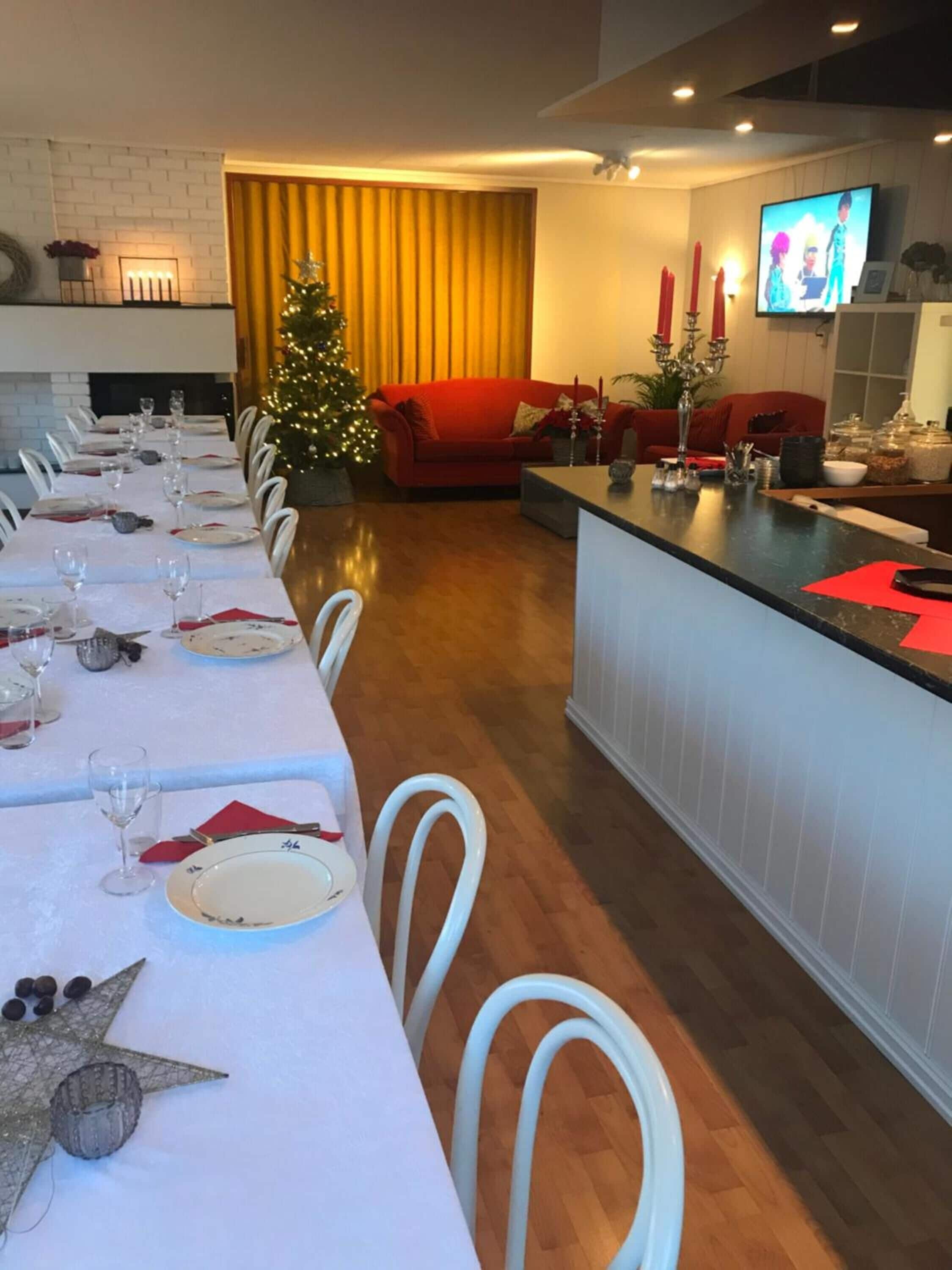 A dining area with a long table set for a meal, a Christmas tree, and a red sofa in the background.